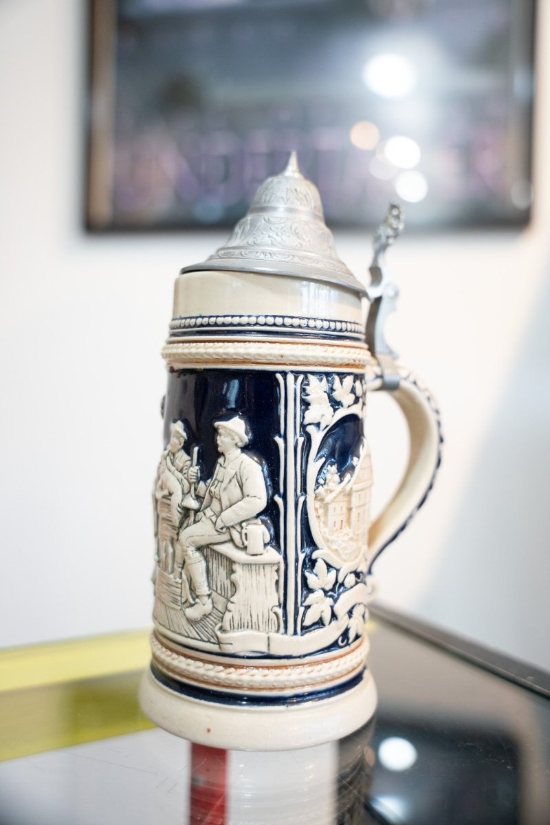Antique German lidded beer stein cobalt blue cream stoneware with Bavarian tavern relief scene village medallion hop vines ornate pewter lid