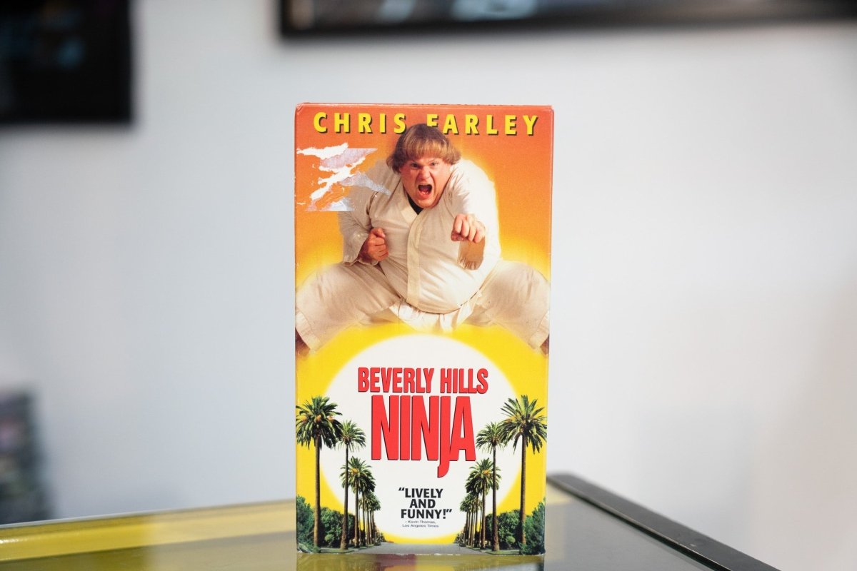 Beverly Hills Ninja VHS orange yellow sleeve with Chris Farley in white ninja gi flying kick palm trees sun yellow red title Lively And Funny quote