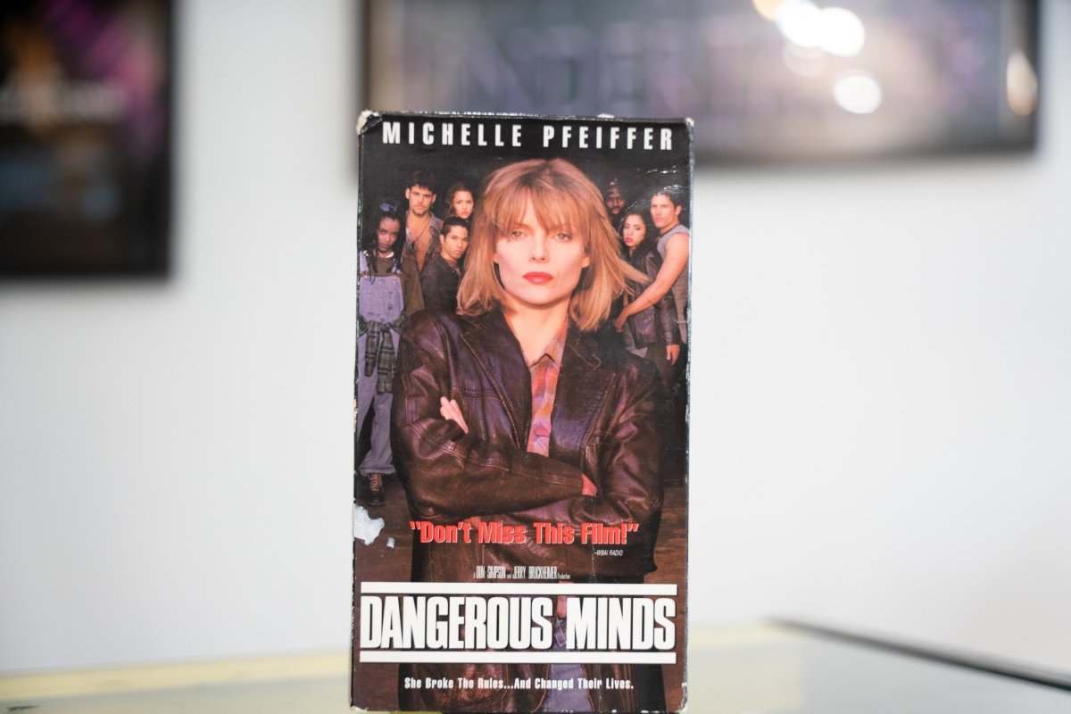 Dangerous Minds VHS dark sleeve with Michelle Pfeiffer in leather jacket arms crossed students behind her white title lettering and Don't Miss This Film quote