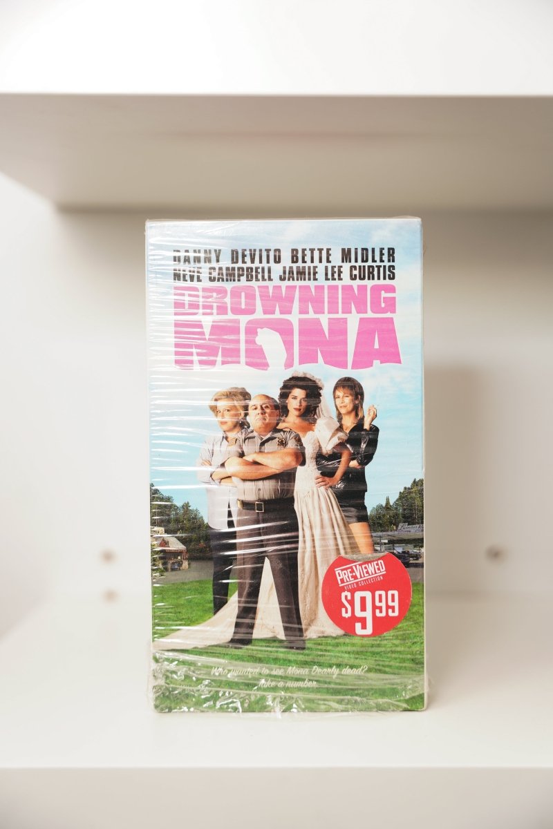 Drowning Mona VHS cover with Danny DeVito, Neve Campbell, Jamie Lee Curtis on green lawn, pink title text, Blockbuster Pre-Viewed sticker