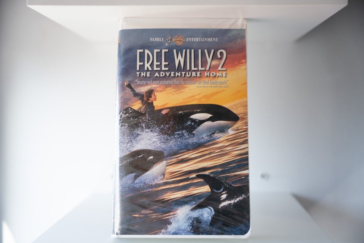 Free Willy 2 The Adventure Home VHS cover showing boy riding orca whale with two more orcas in sunset ocean, Warner Bros Family Entertainment