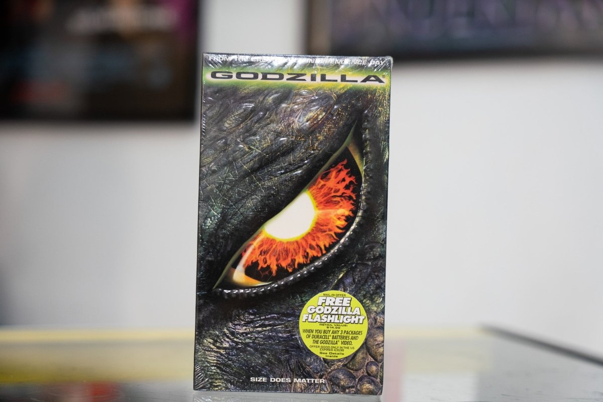 Sealed Godzilla 1998 VHS with massive close-up of Godzilla eye fiery orange iris green metallic title SIZE DOES MATTER tagline and flashlight offer sticker