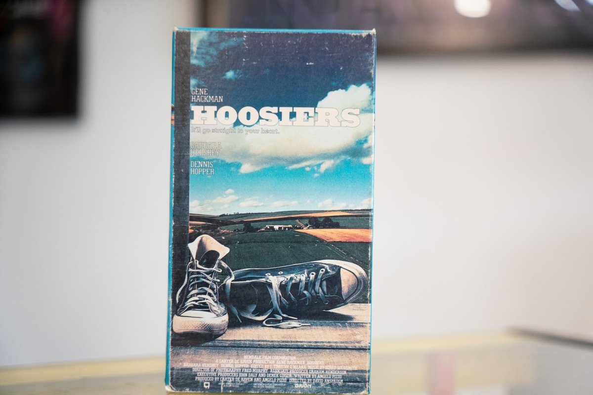 Hoosiers VHS with blue Indiana sky worn black Converse sneakers on wood white HOOSIERS title Gene Hackman Barbara Hershey Dennis Hopper Hemdale