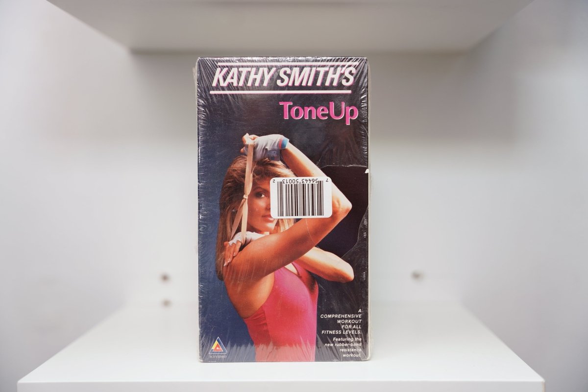 Kathy Smith's Tone Up VHS cover with Smith in pink leotard stretching resistance band, sealed in shrink wrap with barcode sticker