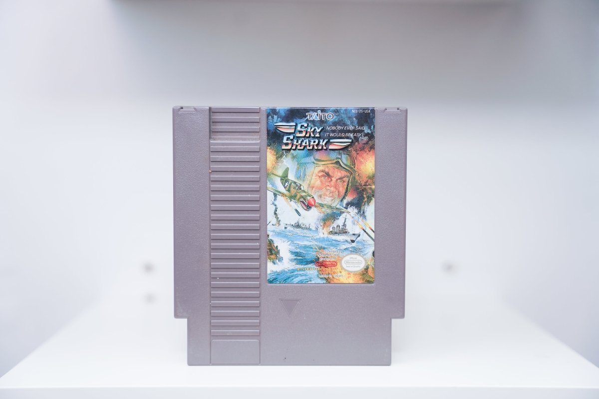 NES Sky Shark grey cartridge with WWII P-40 fighter plane with shark mouth nose art dive-bombing over ocean, Taito logo