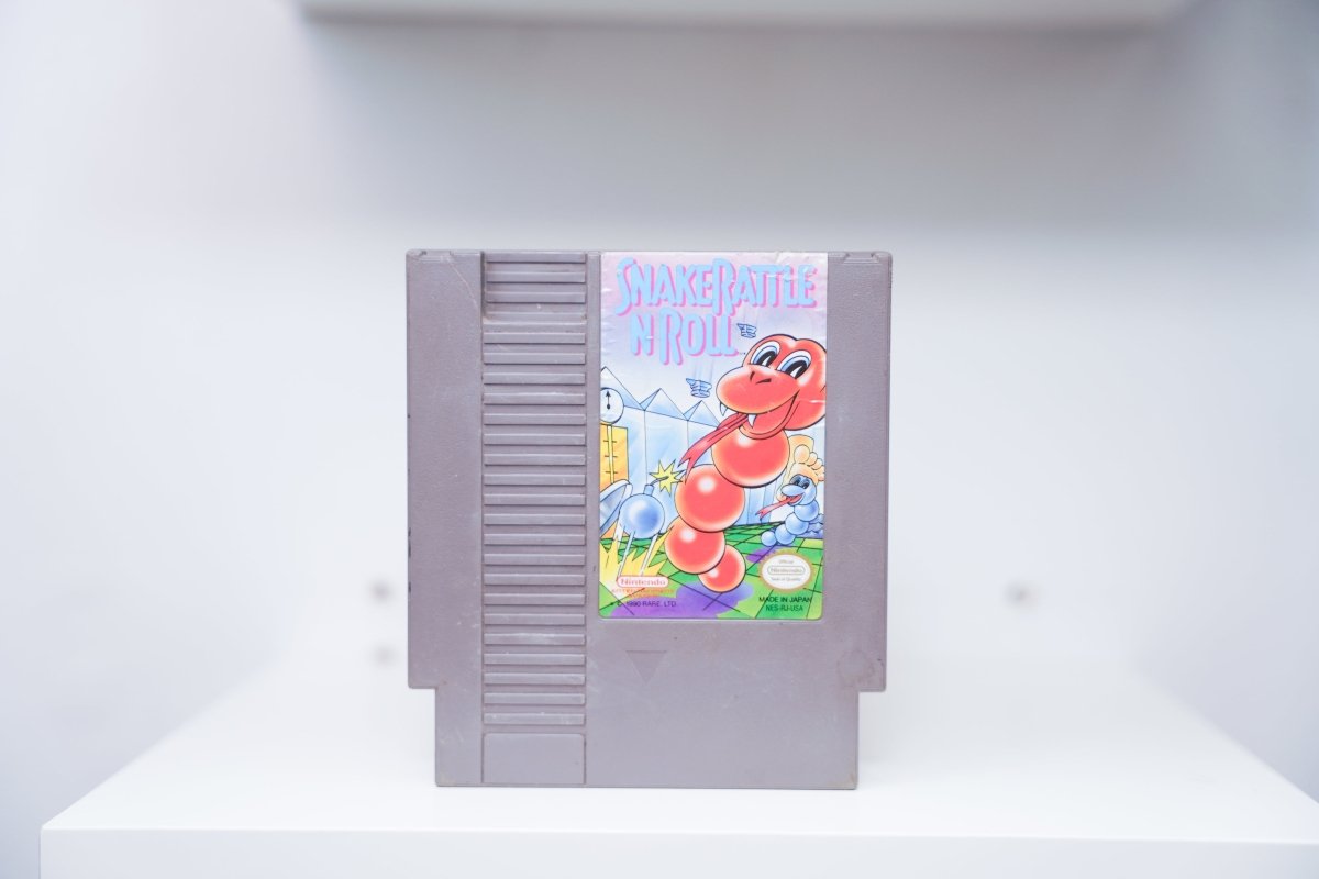 NES Snake Rattle N Roll grey cartridge with colorful cartoon red and blue snakes in whimsical landscape, Rare Ltd copyright, Nintendo logo