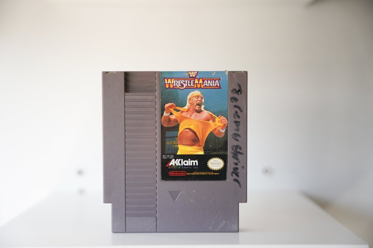 NES WWF WrestleMania gray cartridge Hulk Hogan ripping yellow shirt WWF logo WrestleMania text Acclaim Nintendo writing on shell