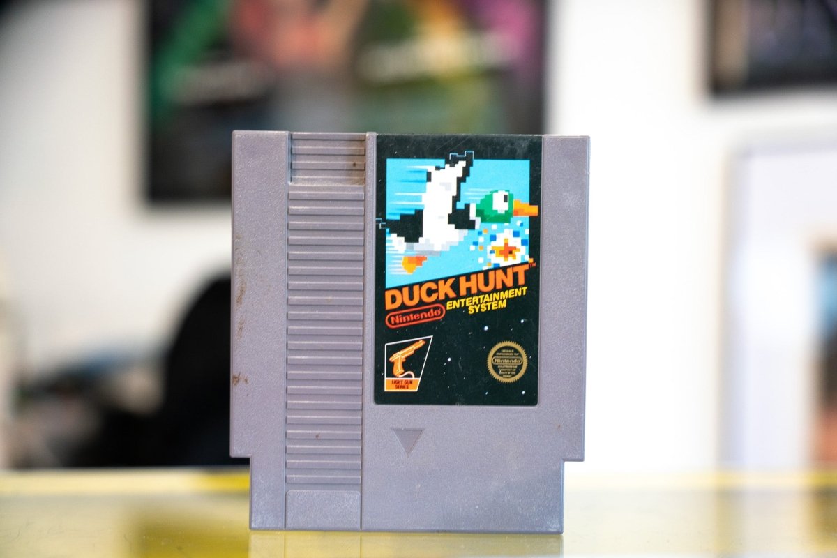 Nintendo NES Duck Hunt gray cartridge with pixelated mallard duck in flight on blue sky and white DUCK HUNT title with Light Gun Series badge