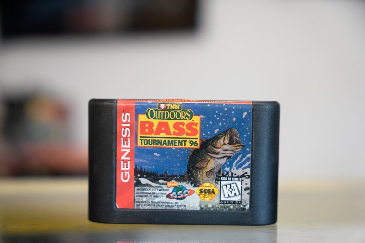 Sega Genesis TNN Outdoors Bass Tournament 96 black cartridge with TNN logo orange OUTDOORS yellow BASS title leaping bass illustration lake backdrop