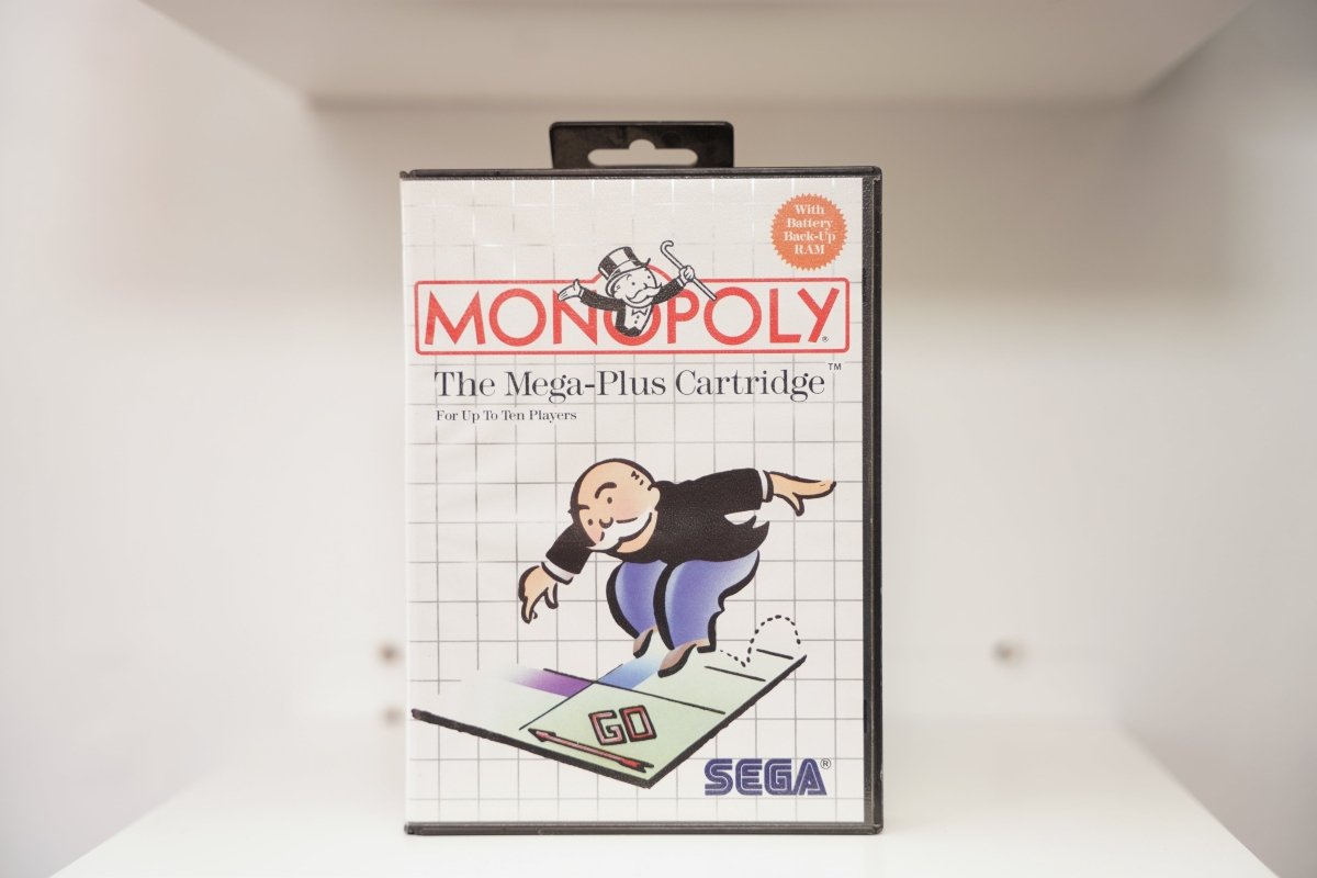 Sega Master System Monopoly clamshell case with Mr. Monopoly striding across GO square, Mega-Plus Cartridge, Battery Back-Up RAM badge