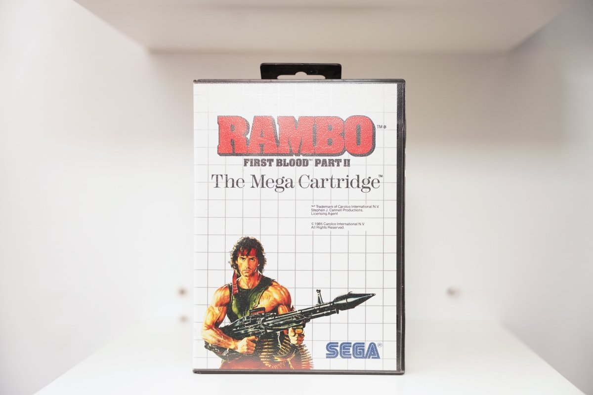 Sega Master System Rambo First Blood Part II clamshell case with illustrated Rambo holding machine gun and ammo belt, The Mega Cartridge subtitle