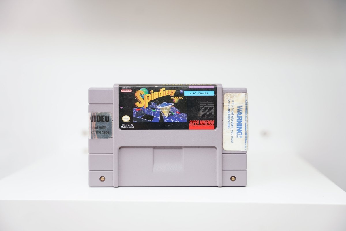 SNES Spindizzy Worlds grey cartridge with geometric craft on isometric platforms, ASCII Ware logo, video rental store stickers