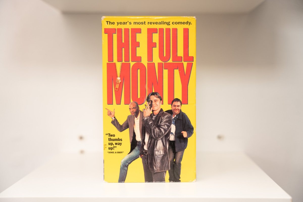 The Full Monty VHS cover with three cast members on yellow background, large red title text, zipper graphic, and Siskel & Ebert quote