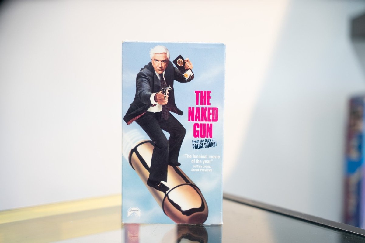 The Naked Gun VHS light blue sleeve Leslie Nielsen suit revolver badge riding giant bullet magenta title From the Files of Police Squad Paramount