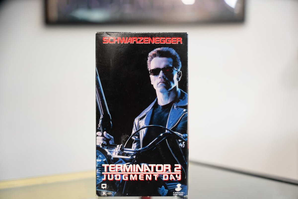 Terminator 2 Judgment Day VHS black sleeve with Schwarzenegger on motorcycle holding shotgun red glowing eye sunglasses red title Carolco Rated R