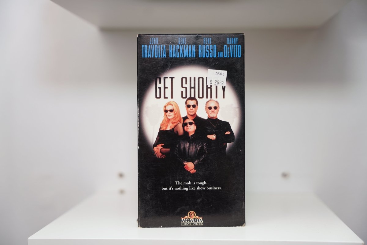 VHS Get Shorty black cover Travolta leather jacket Russo DeVito Hackman sunglasses spotlight GET SHORTY gold text mob tagline MGM/UA