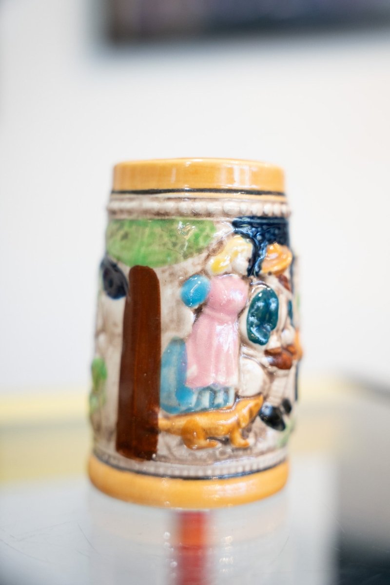 Vintage German mini beer stein colorful hand-painted ceramic with woman in pink dress dog village scene amber rim brown handle no lid