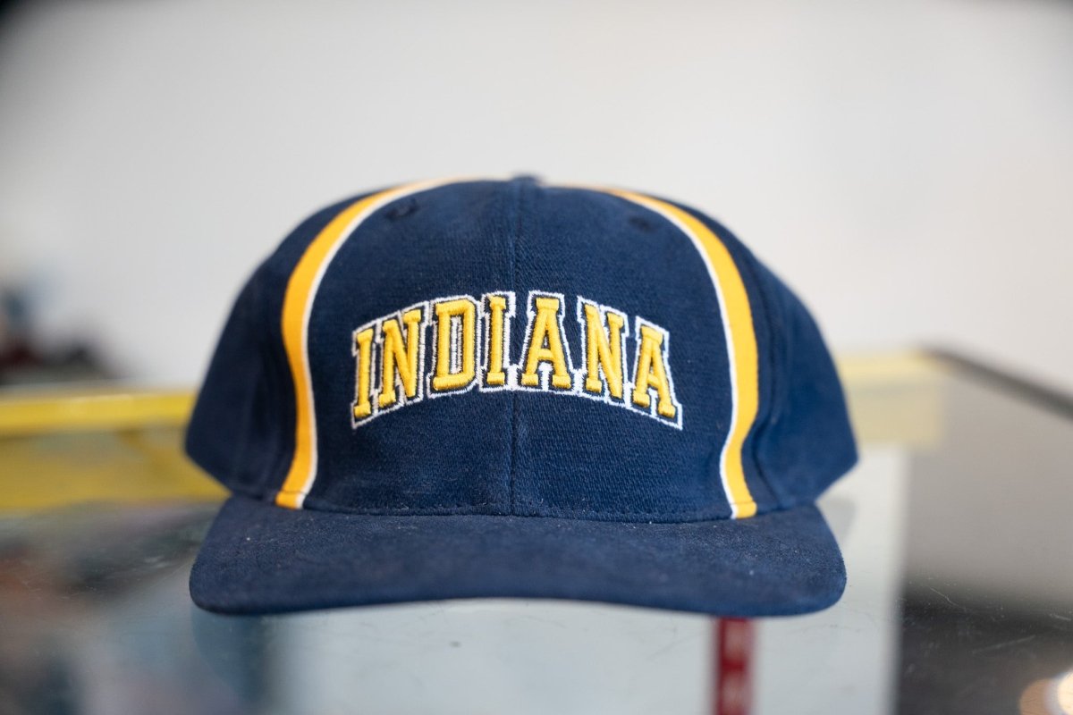 Navy vintage Indiana Pacers snapback hat with large gold embroidered arched INDIANA lettering white outline and gold white piping stripes on crown