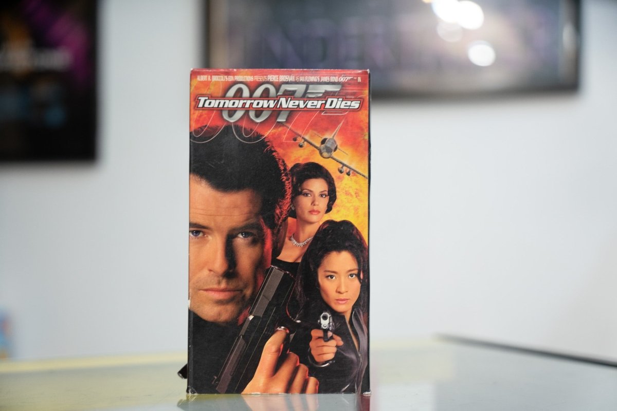 007 Tomorrow Never Dies VHS with Pierce Brosnan holding pistol Teri Hatcher Michelle Yeoh fiery explosion background and white italic title