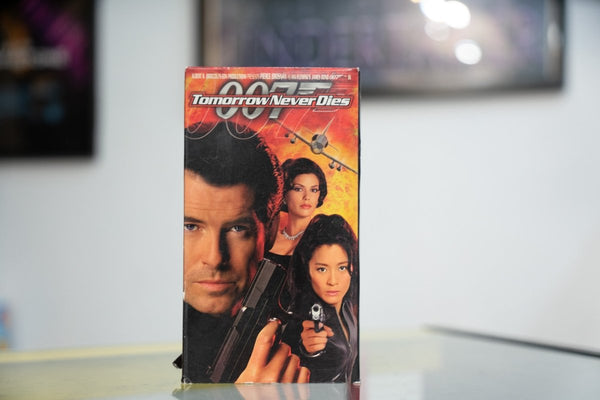 007 Tomorrow Never Dies VHS with Pierce Brosnan holding pistol Teri Hatcher Michelle Yeoh fiery explosion background and white italic title