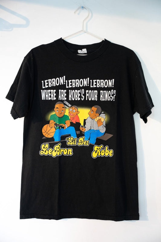 Black 2009 Kobe Lil Dez LeBron tee with cartoon illustration WHERE ARE KOBE'S FOUR RINGS text LeBron Lil Dez Kobe characters yellow script size Medium