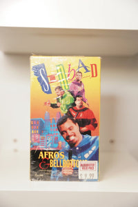 VHS Sinbad Afros and Bellbottoms bright yellow orange cover SINBAD multicolor text multiple poses colorful outfits city background Blockbuster sticker