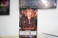 Dangerous Minds VHS dark sleeve with Michelle Pfeiffer in leather jacket arms crossed students behind her white title lettering and Don't Miss This Film quote