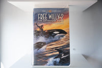 Free Willy 2 The Adventure Home VHS cover showing boy riding orca whale with two more orcas in sunset ocean, Warner Bros Family Entertainment