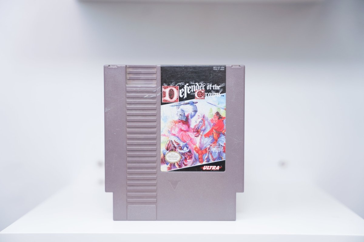 NES Defender of the Crown grey cartridge with medieval knights jousting on horseback, ornate Celtic-style title lettering, Ultra Games logo