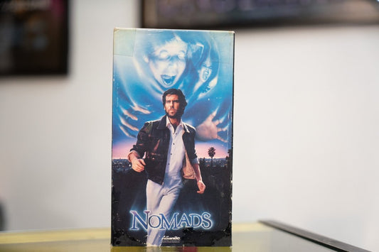 Nomads VHS blue-toned sleeve with Pierce Brosnan in leather jacket LA skyline ghostly screaming figure above silver NOMADS title Atlantic Releasing
