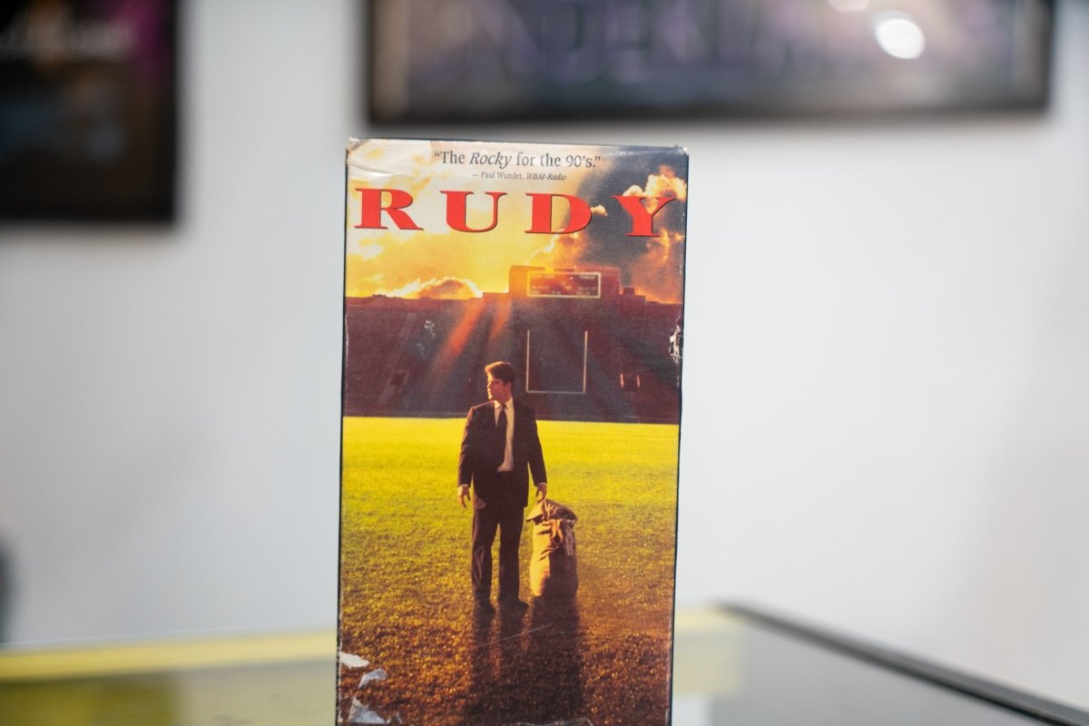 Rudy VHS golden-toned sleeve with Sean Astin in suit on Notre Dame football field at sunset red RUDY title and Rocky for the 90s quote