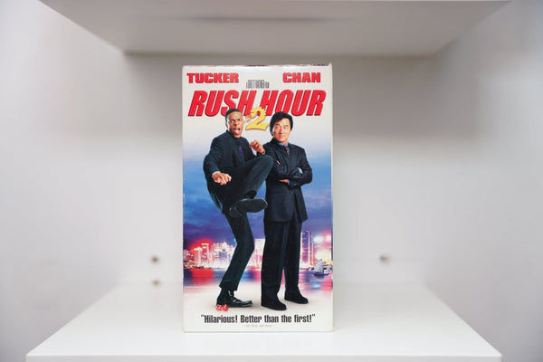 Rush Hour 2 VHS cover with Chris Tucker kicking and Jackie Chan arms crossed against neon Hong Kong skyline, bold red title text