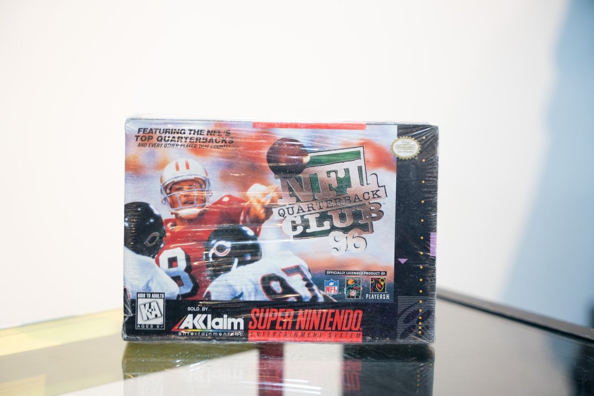 SNES NFL Quarterback Club 96 box with quarterback in red jersey throwing pass, Acclaim logo, NFL licenses, appears sealed in shrink wrap