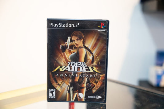 PlayStation 2 Lara Croft Tomb Raider Anniversary black PS2 case Lara dual pistol pose golden artifacts TOMB RAIDER gold text Eidos Teen