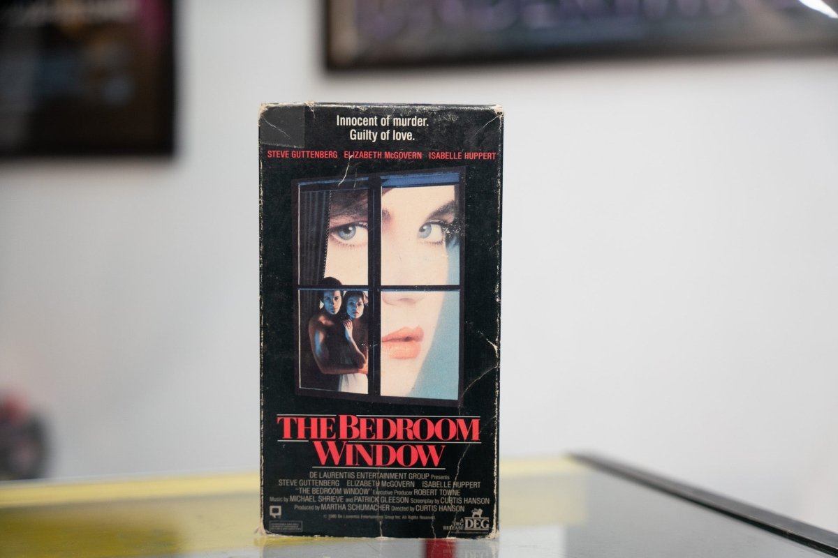 The Bedroom Window VHS dark sleeve with woman looking through window panes couple embracing behind glass red title Innocent of murder Guilty of love tagline