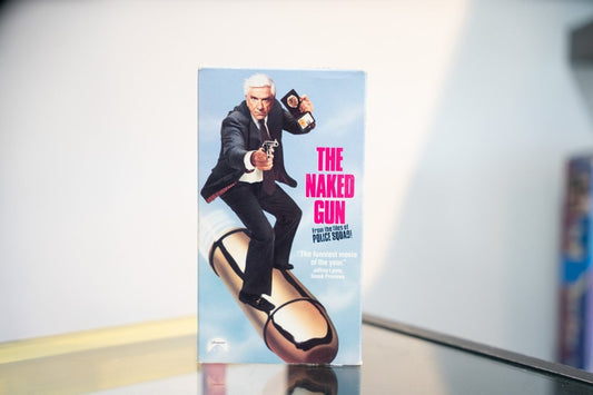 The Naked Gun VHS light blue sleeve Leslie Nielsen suit revolver badge riding giant bullet magenta title From the Files of Police Squad Paramount