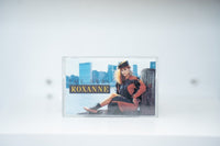 The Real Roxanne cassette tape clear case Roxanne on NYC waterfront dock pilings Manhattan skyline orange black outfit THE REAL ROXANNE text
