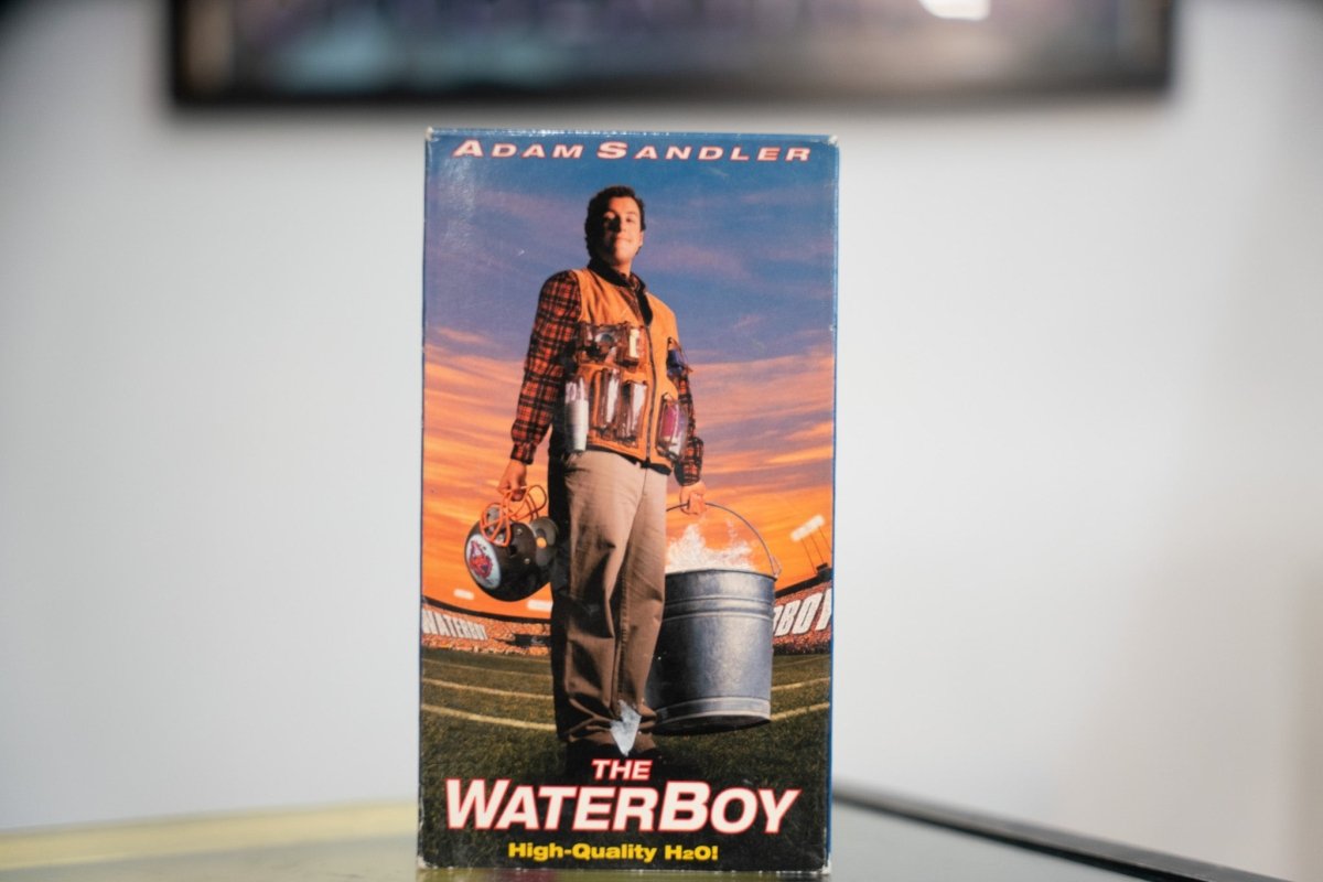 The Waterboy VHS blue sky sleeve with Adam Sandler in plaid shirt orange vest water bottles football field sunset white red title High Quality H2O tagline