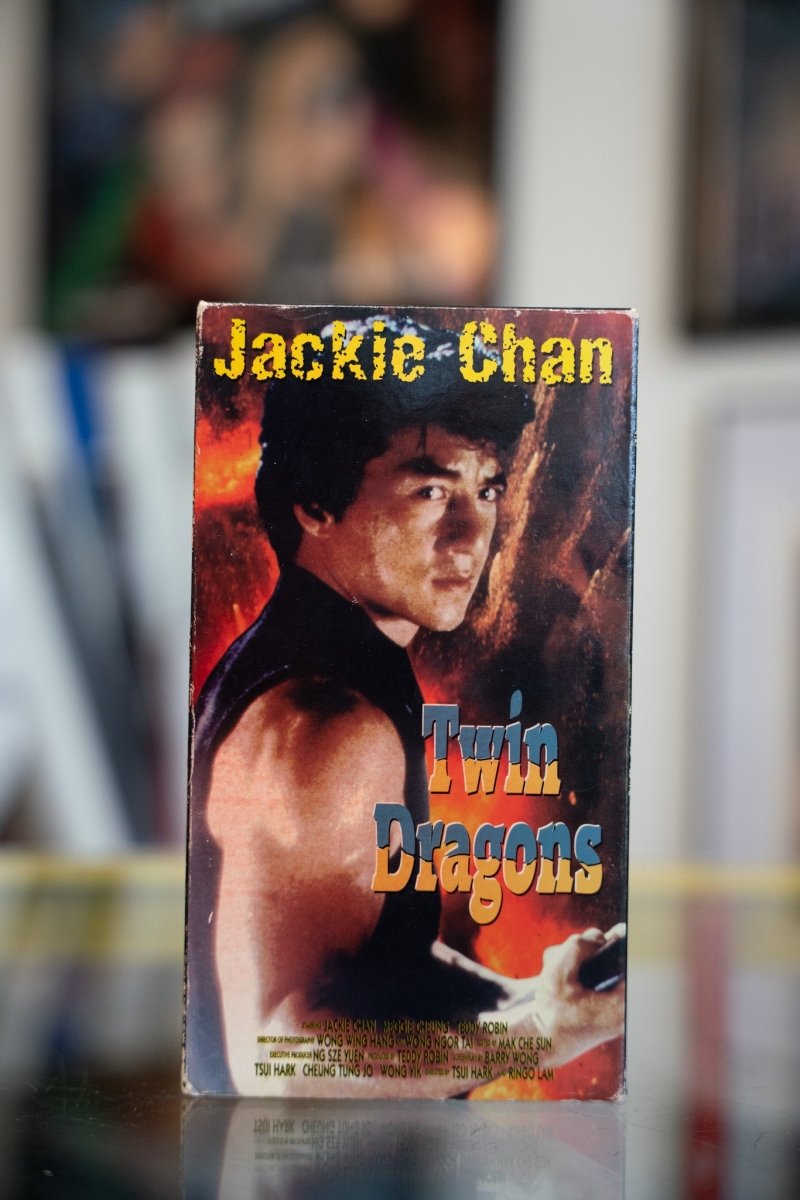 Twin Dragons VHS tape with shirtless Jackie Chan against fiery explosion background with yellow name and blue gold title script