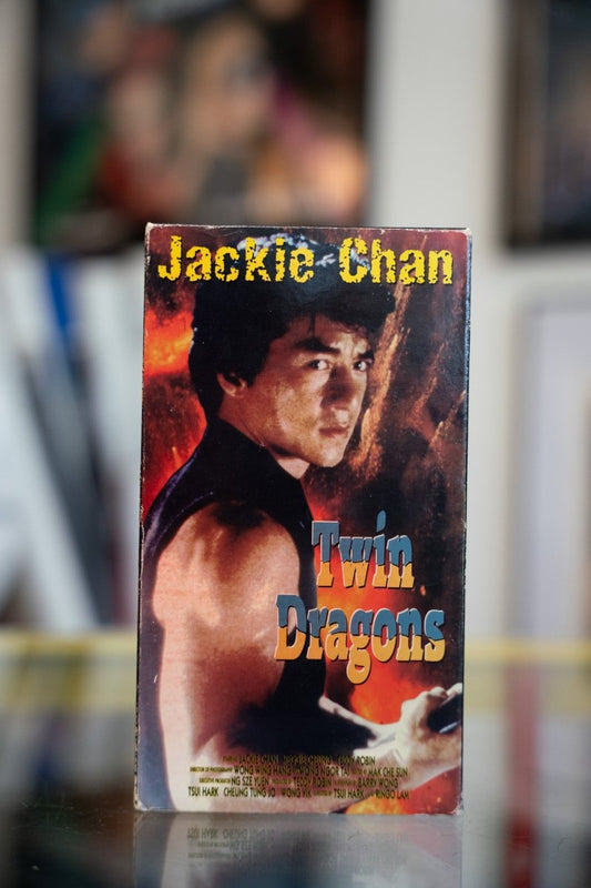 Twin Dragons VHS tape with shirtless Jackie Chan against fiery explosion background with yellow name and blue gold title script