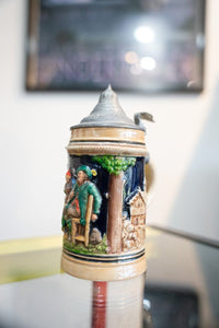Collectible vintage German beer stein with ceramic body, decorative lid, and painted details showing traditional design elements
