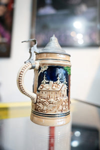 Collectible German beer stein with blue and white ceramic body, pewter lid, and decorative relief pattern showing traditional design elements