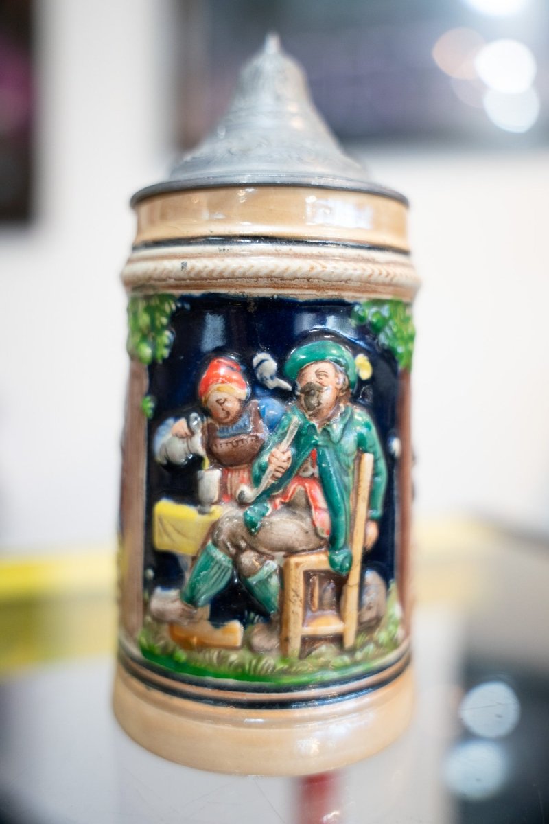Vintage German beer stein cobalt blue with colorful Bavarian musicians relief scene green jacket red cap hop vines pewter lid pointed finial
