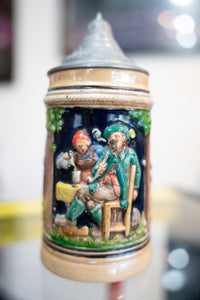 Vintage German beer stein cobalt blue with colorful Bavarian musicians relief scene green jacket red cap hop vines pewter lid pointed finial