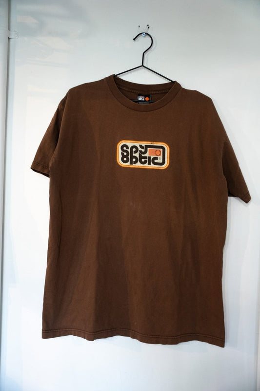 Brown vintage Spy Optic shirt with centered mirrored SPY logo in rounded rectangle with orange accent on chest