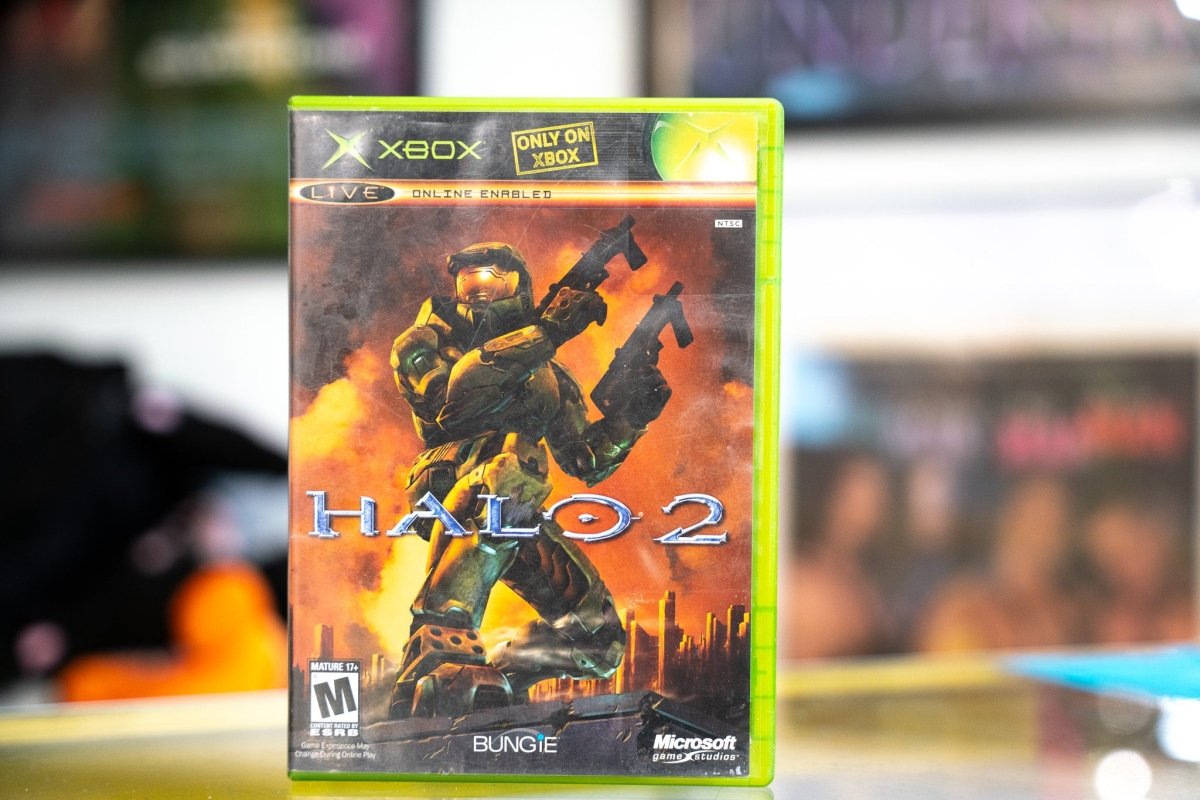 Xbox Halo 2 green case with Master Chief in Mjolnir armor dual-wielding weapons against fiery explosion backdrop and silver HALO 2 title